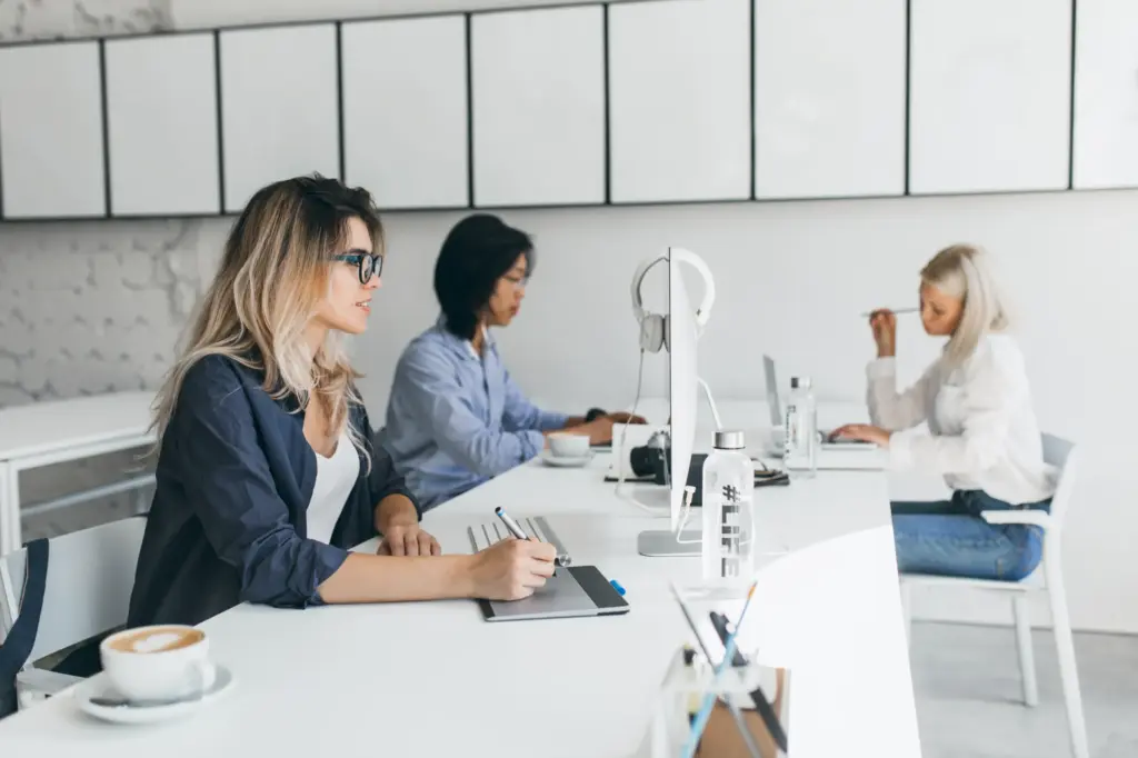 Drei Frauen sitzen an einem Schreibtisch und arbeiten jeweils am PC.